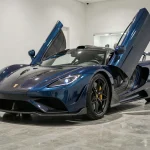 Koenigsegg Agera R bleu nuit exposée dans un showroom privé, vue trois quarts avant sur carrosserie en fibre de carbone