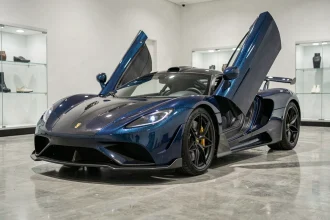 Koenigsegg Agera R bleu nuit exposée dans un showroom privé, vue trois quarts avant sur carrosserie en fibre de carbone